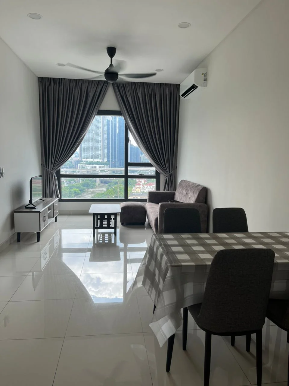 Living features: grey fabric sofa, coffee table, TV console, wall-mounted TV, 5-blade ceiling fan with light, floor-to-ceiling windows, grey curtains, white painted walls, glossy ceramic tile flooring, dining table with checkered tablecloth, 4 upholstered dining chairs, air conditioning unit; style: modern; view: city.